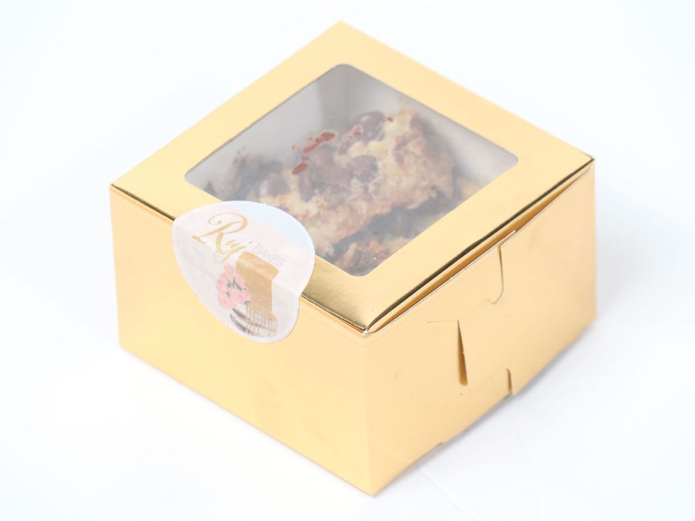 Gold retail bakery boxes with transparent window displays arranged in a row.