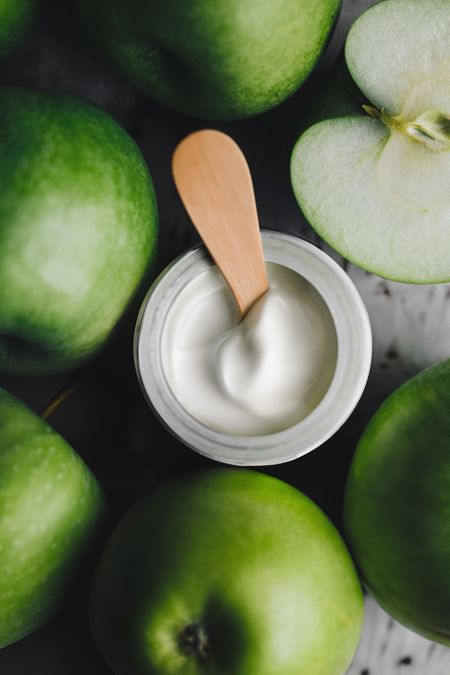 Detaljbild av Juice Beauty ansiktskräm med träspatel i burken, omringad av gröna äpplen