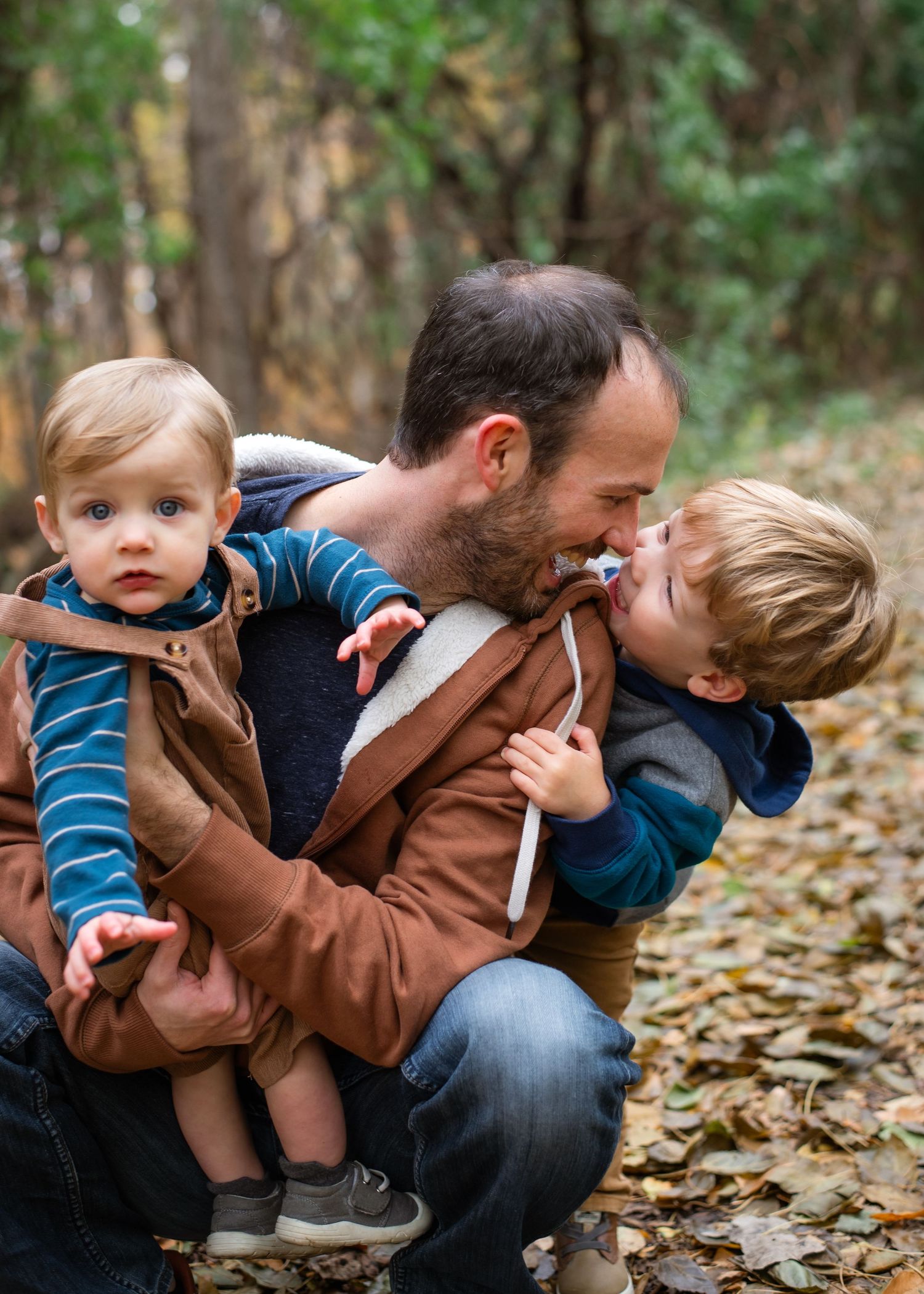 A family stands together on an autumn path covered in fallen leaves while wearing coordinating blue and neutral outfits.