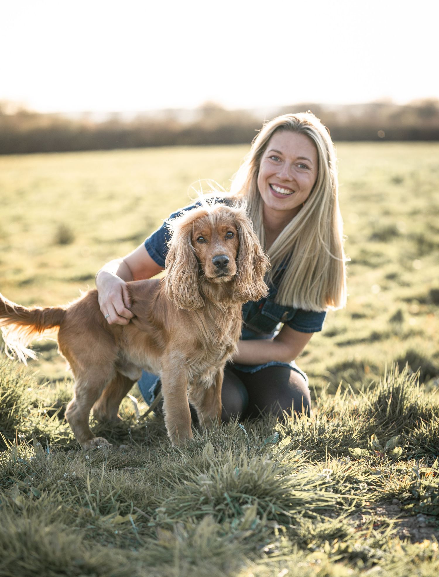 A golden retriever and their companion pose together in a sunlit meadow during golden hour for a heartwarming photoshoot.