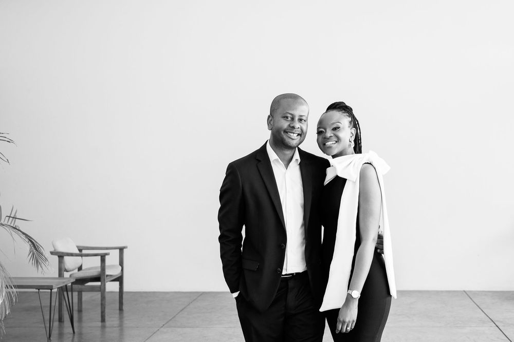 Two people wearing formal attire pose together in black and white with happy expressions in matching outfits.
