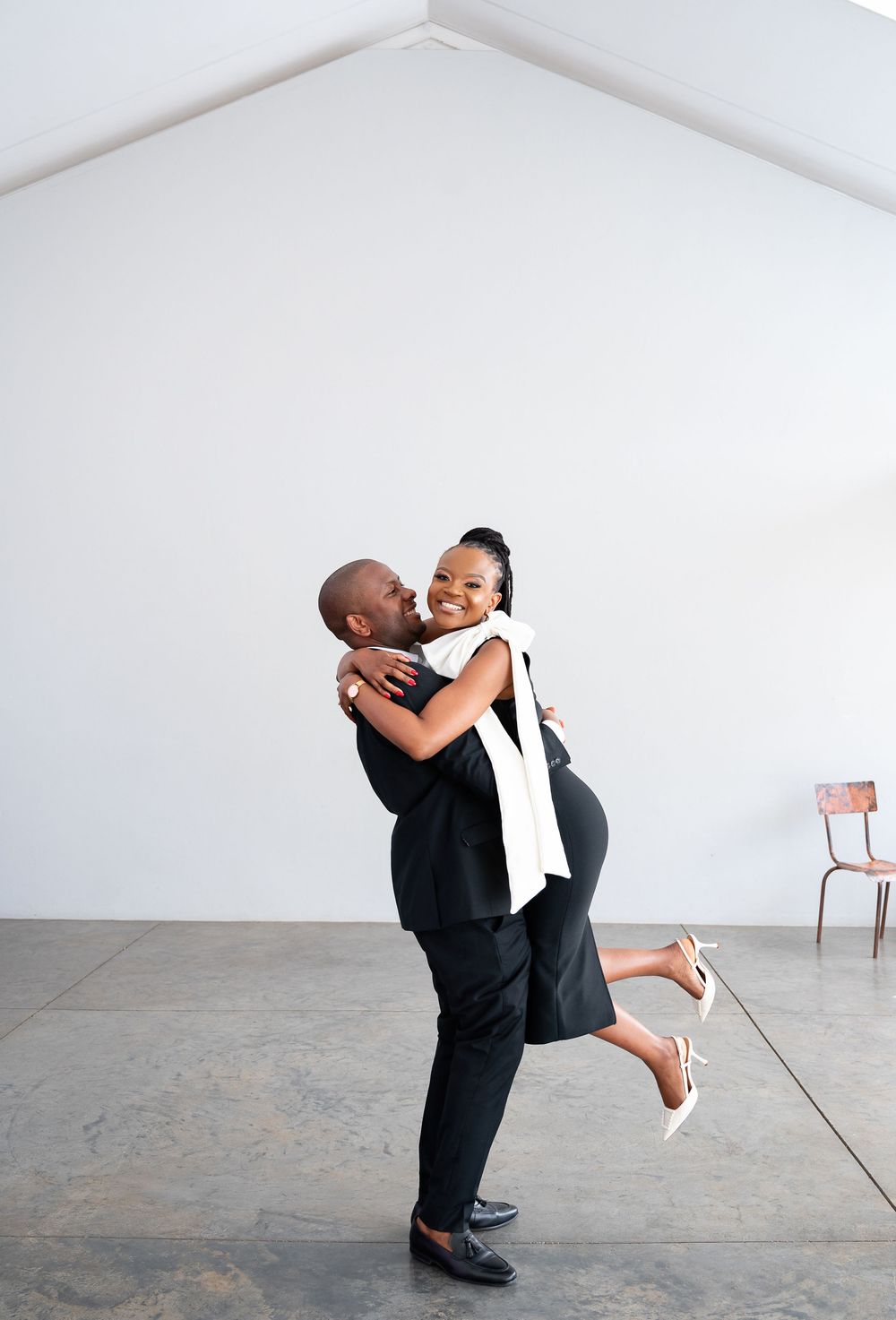 Couple shares a joyful embrace in a minimalist white room with concrete floors.