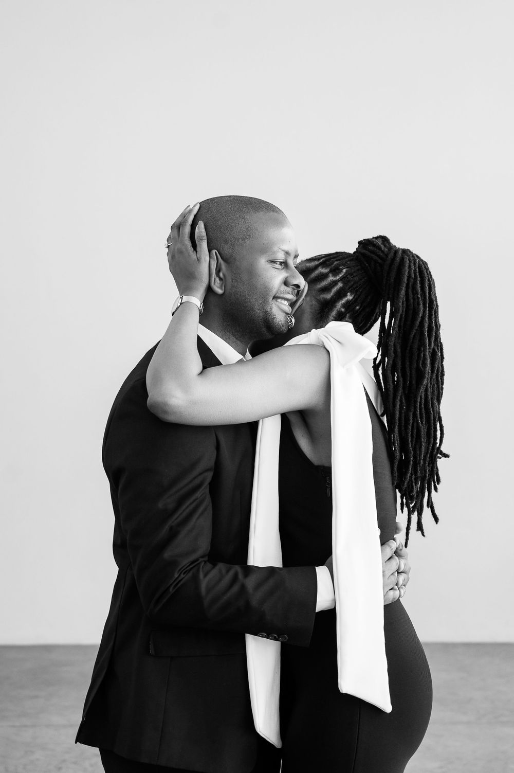 A romantic couple embraces in elegant black and white attire against a light backdrop.