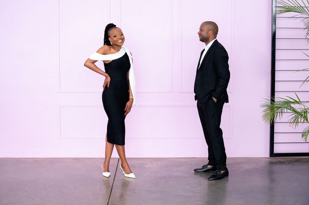 Two people dancing together in a rehearsal studio with white walls and wood flooring.