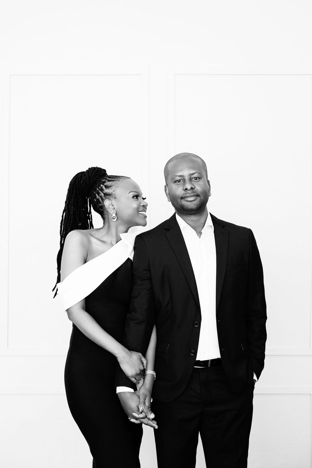 Contemporary black and white studio portraits of a stylish couple in formal attire posing intimately against white backdrop.