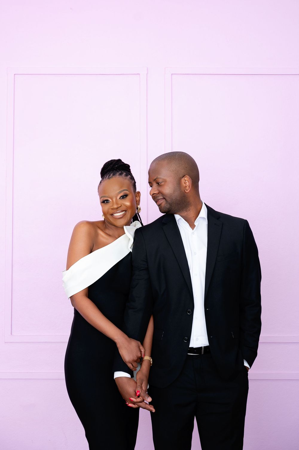A couple in formal black and white attire share intimate poses against a pink background.