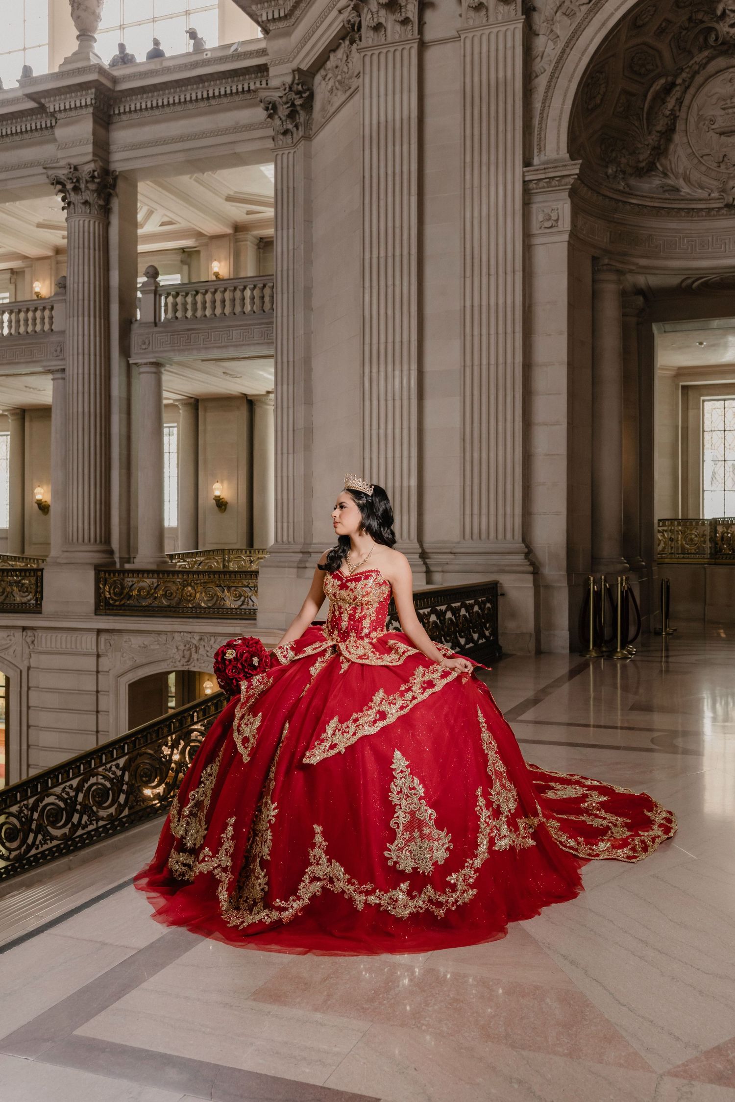 Stunning red ballgown with gold embellishments photographed in an elegant marble hall with classical columns.