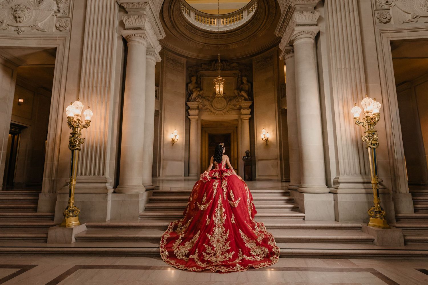 Opulent ballroom interior featuring red and black formal dresses against white marble columns.