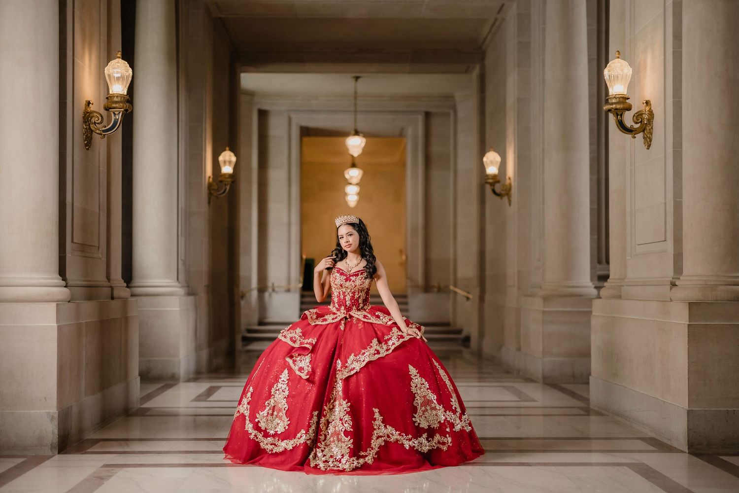 A group of elegant red dresses with gold embellishments displayed in a grand, ornate palace hallway.