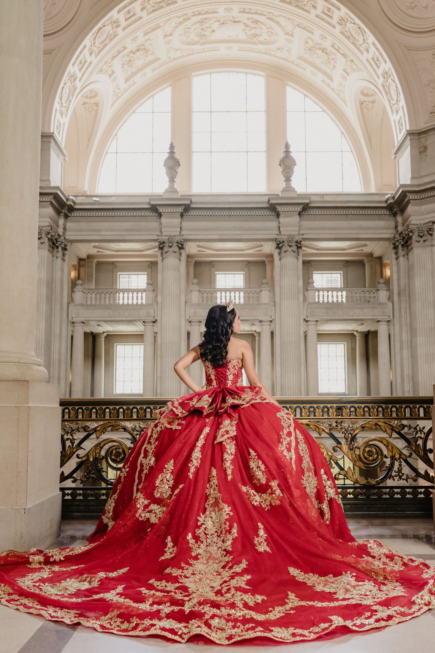 Stunning red and gold embroidered ballgown with cathedral train photographed in elegant marble hallway with arched windows.
