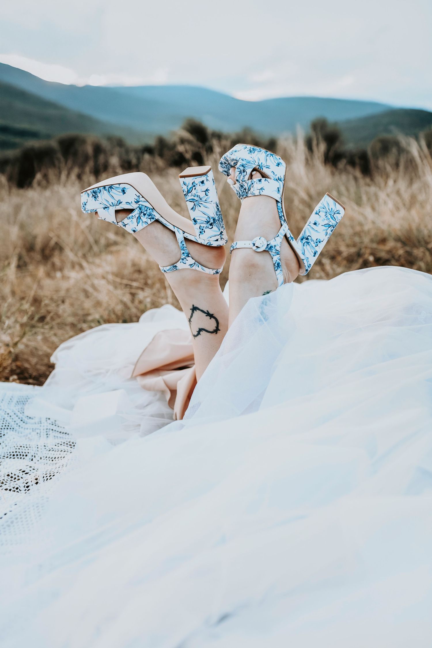 Bride with vintage-inspired shoes and embroidered veil standing in grassy Texas hillside.