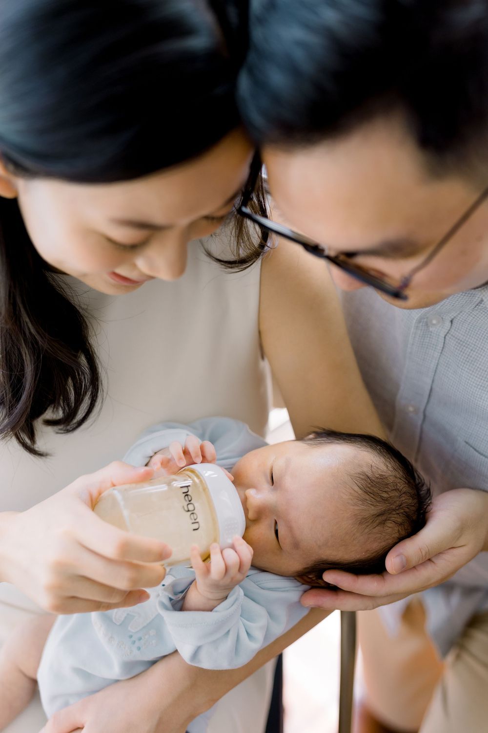 Parents lovingly feed their newborn baby with a bottle while sharing an intimate family moment together.