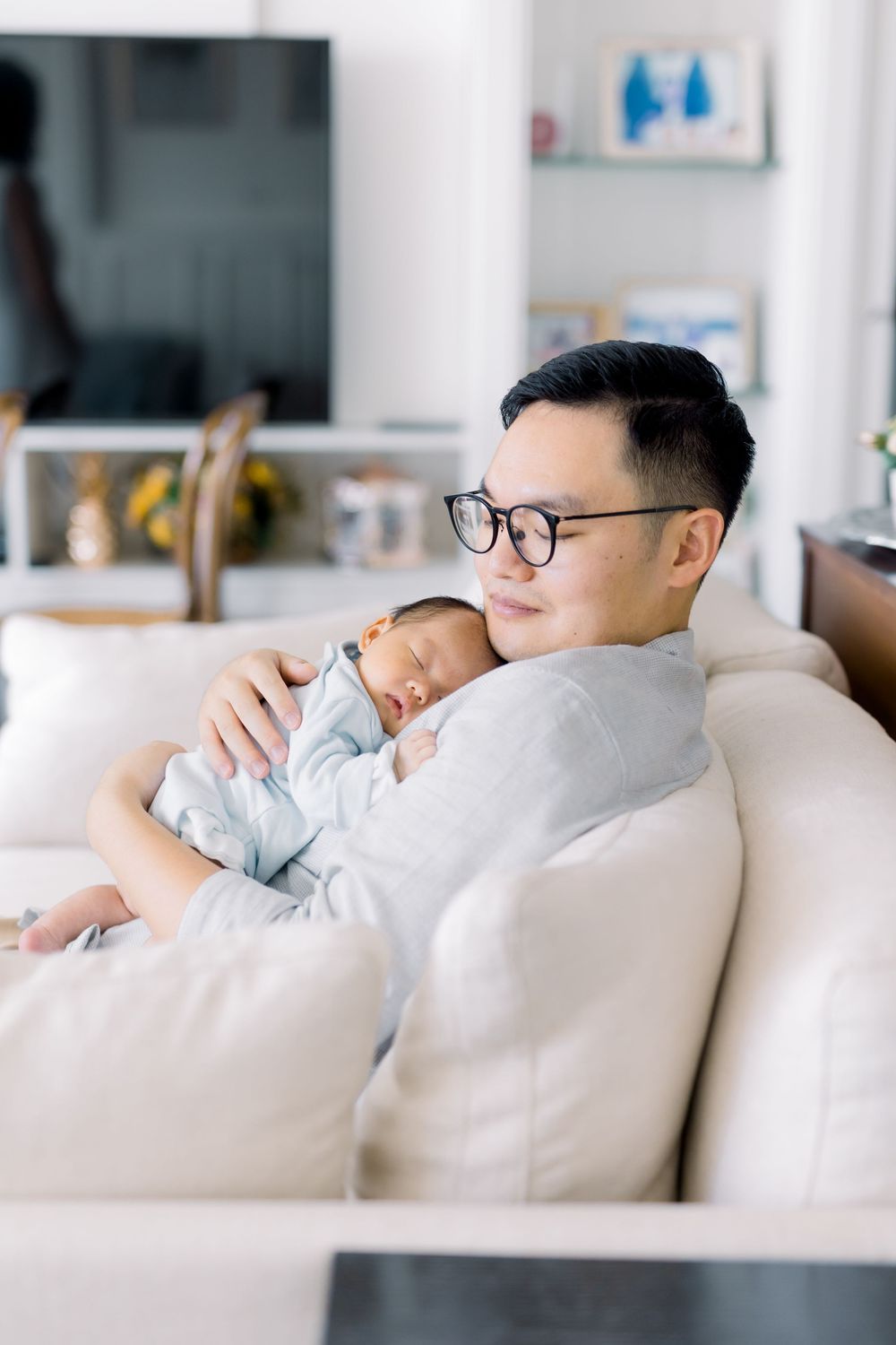 A peaceful moment as a baby sleeps soundly on a parent's shoulder while resting on a white couch at home.