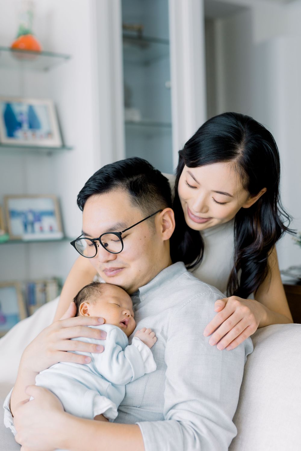 An intimate family portrait showing parents sharing a gentle moment with their sleeping newborn in a cozy home setting.