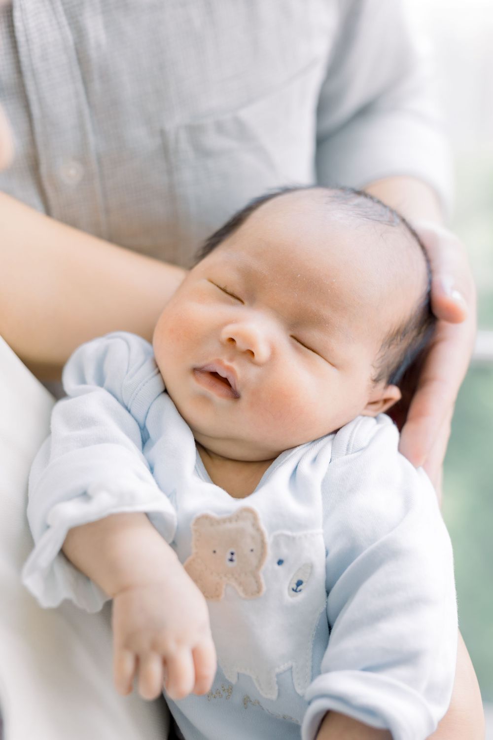 A sleeping newborn baby wearing white clothing rests peacefully in soft lighting.