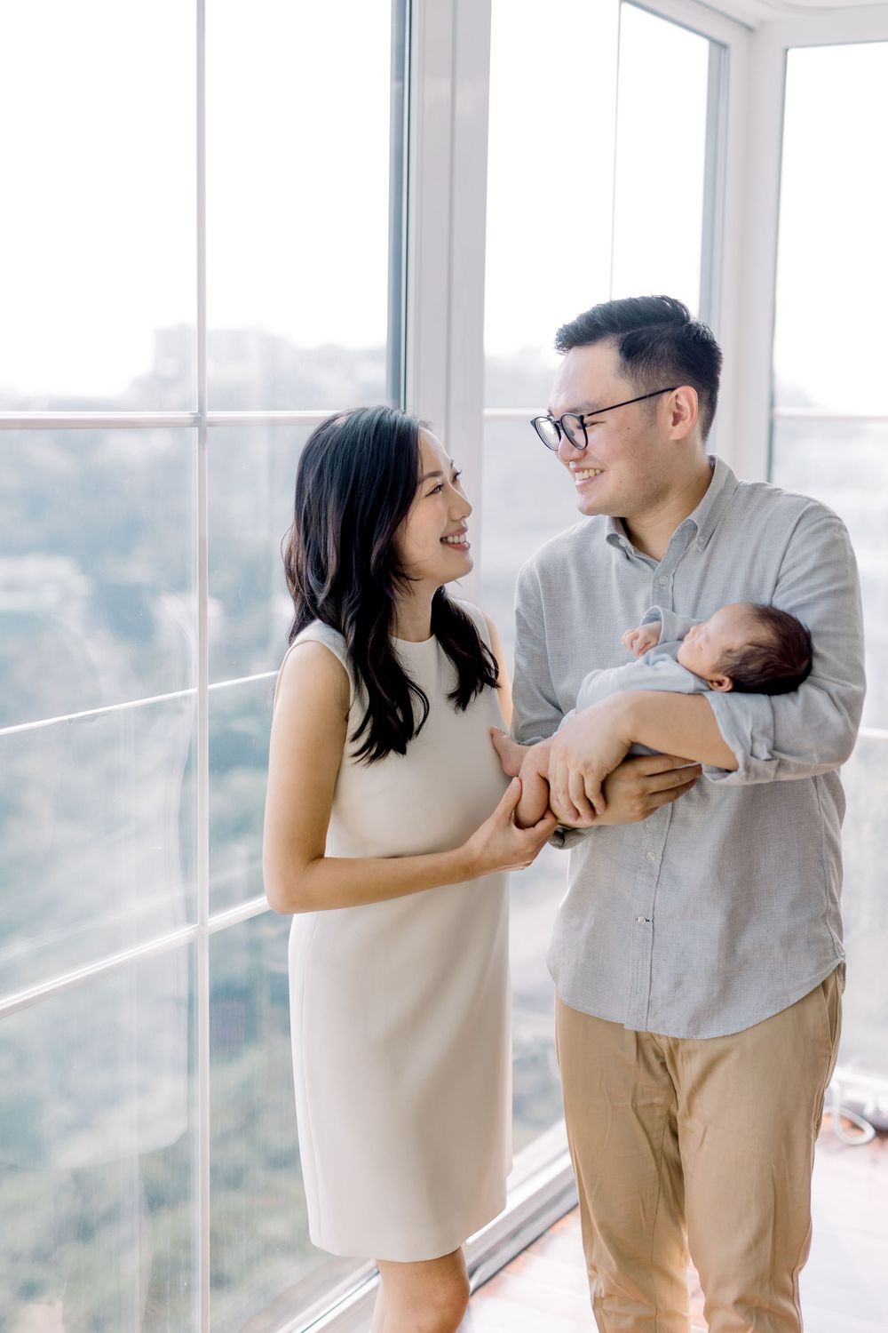 A couple shares joyful laughter together while standing by bright windows in a modern interior space.