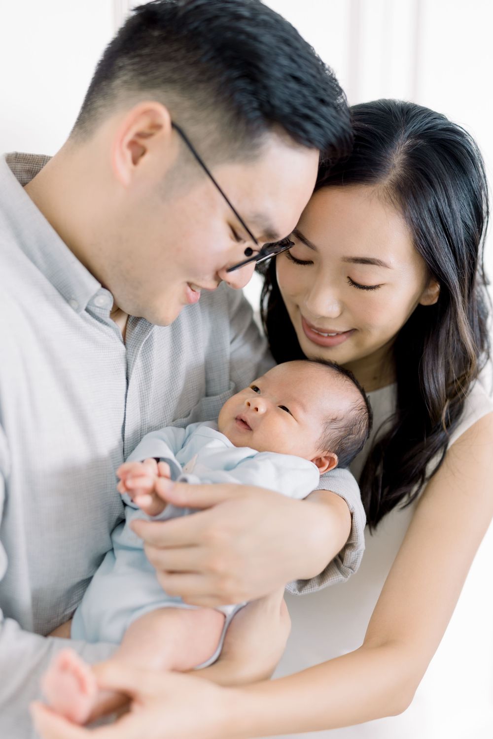 Parents in white outfits lovingly embrace their newborn baby in a tender studio photoshoot sequence.