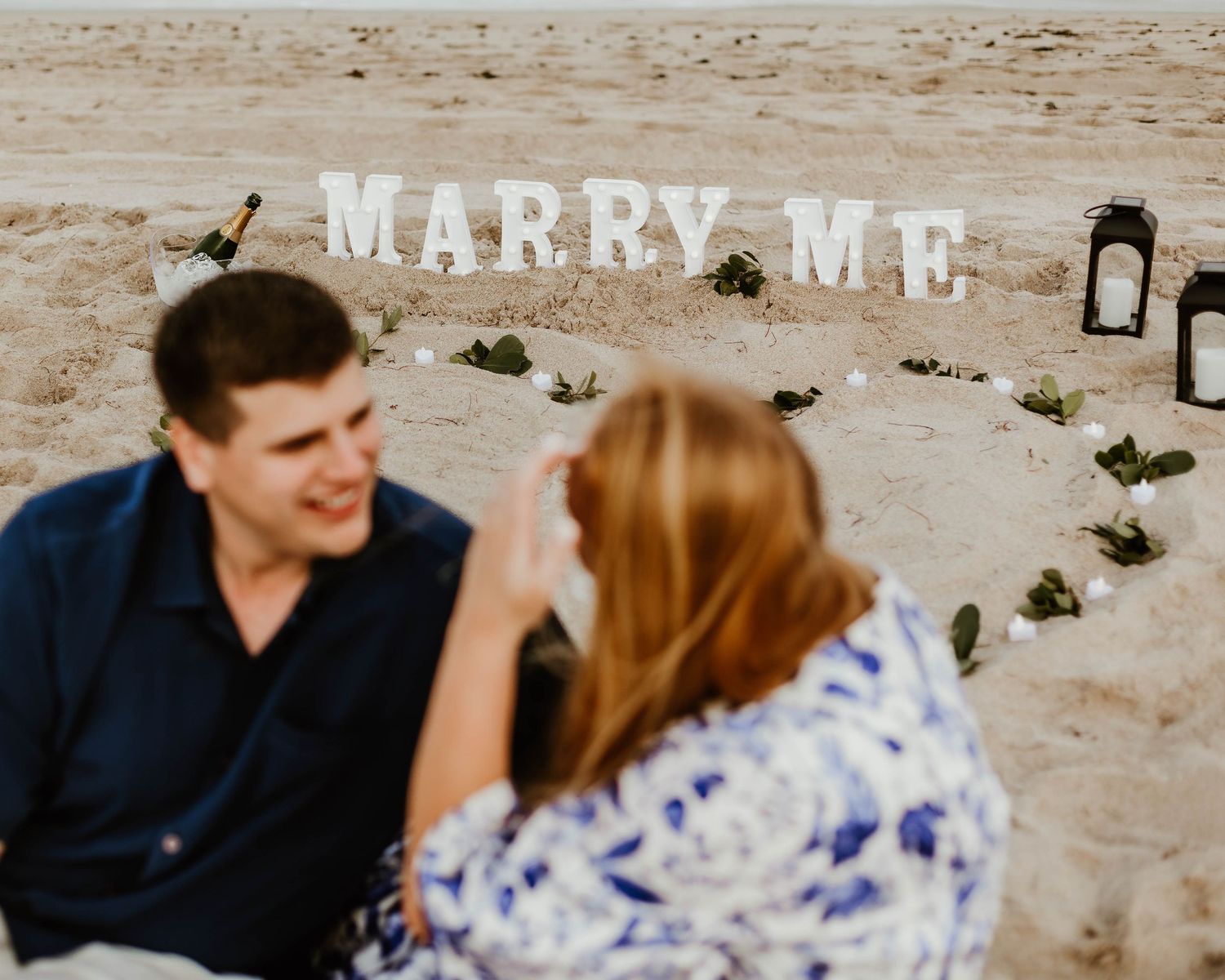Marriage proposal setup on sandy beach with text spelling out 'Marry Me'.