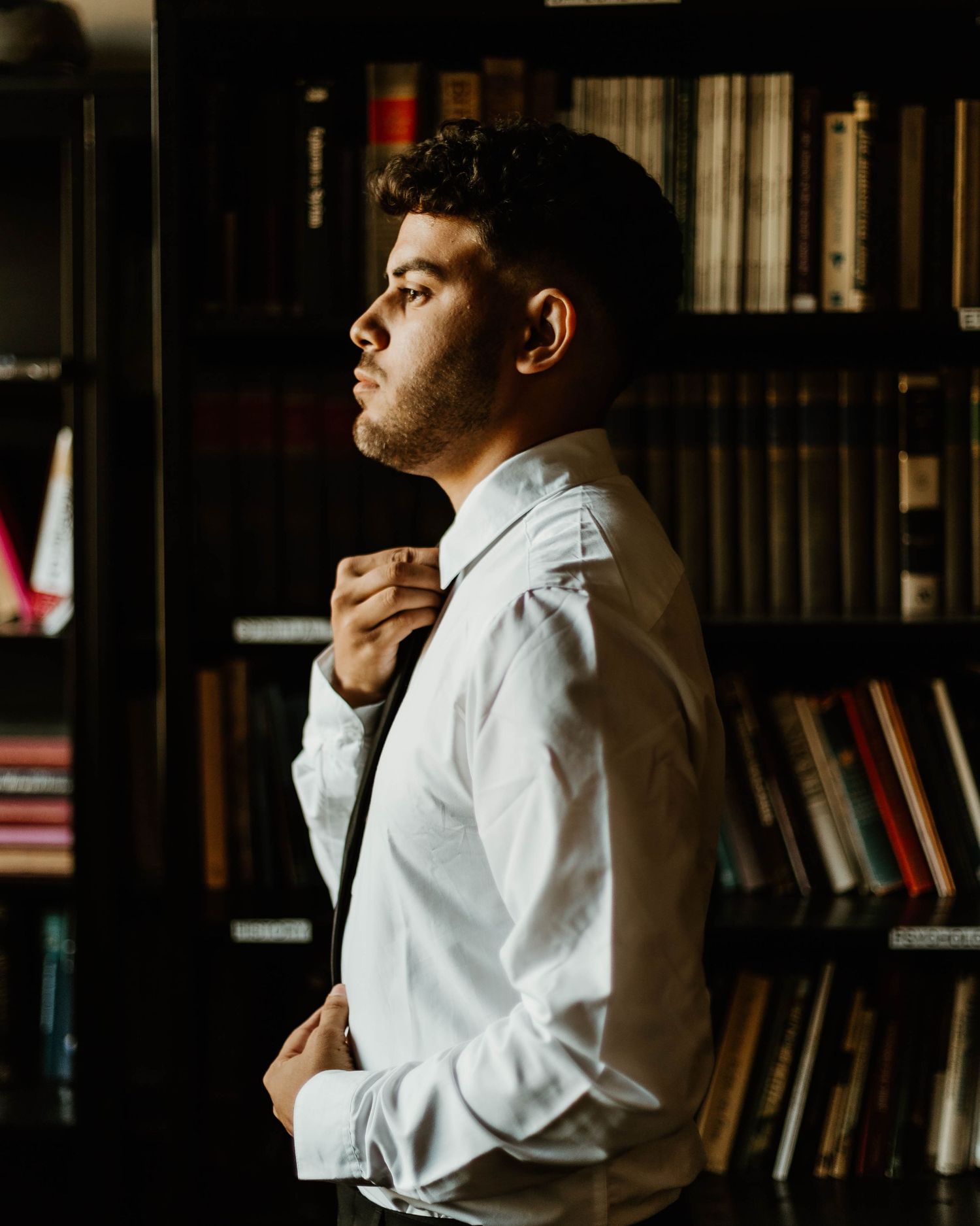 Atmospheric portrait in library with dramatic lighting and bookshelves.