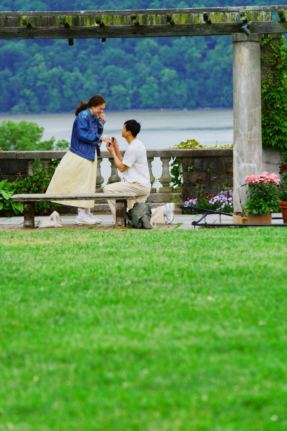 People enjoy a romantic moment on a wooden bench overlooking a scenic lake surrounded by lush green landscape. Wave hill garden
