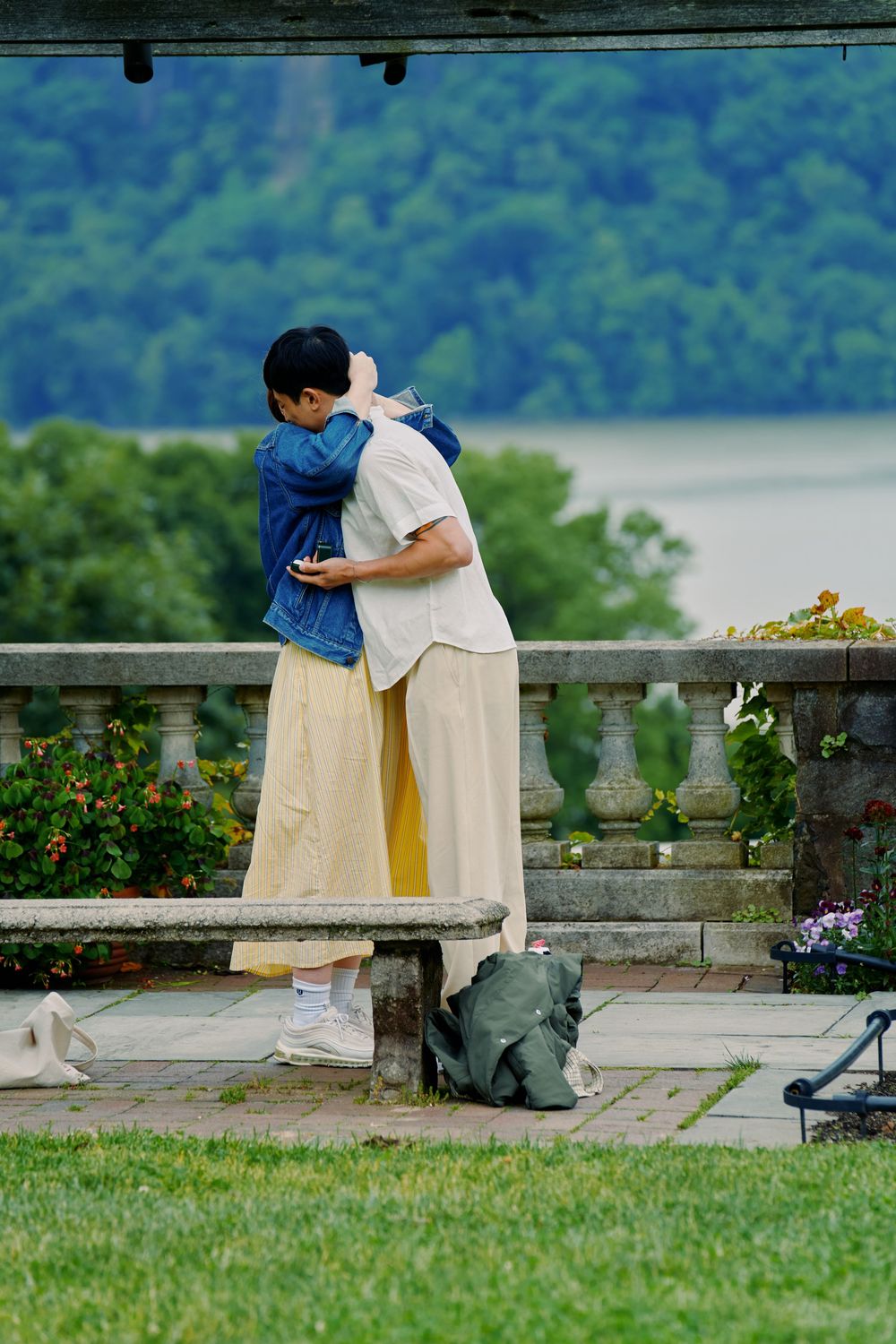 Two people sit close together on a stone bench overlooking a scenic mountain landscape on a sunny summer day. Wave hill garden