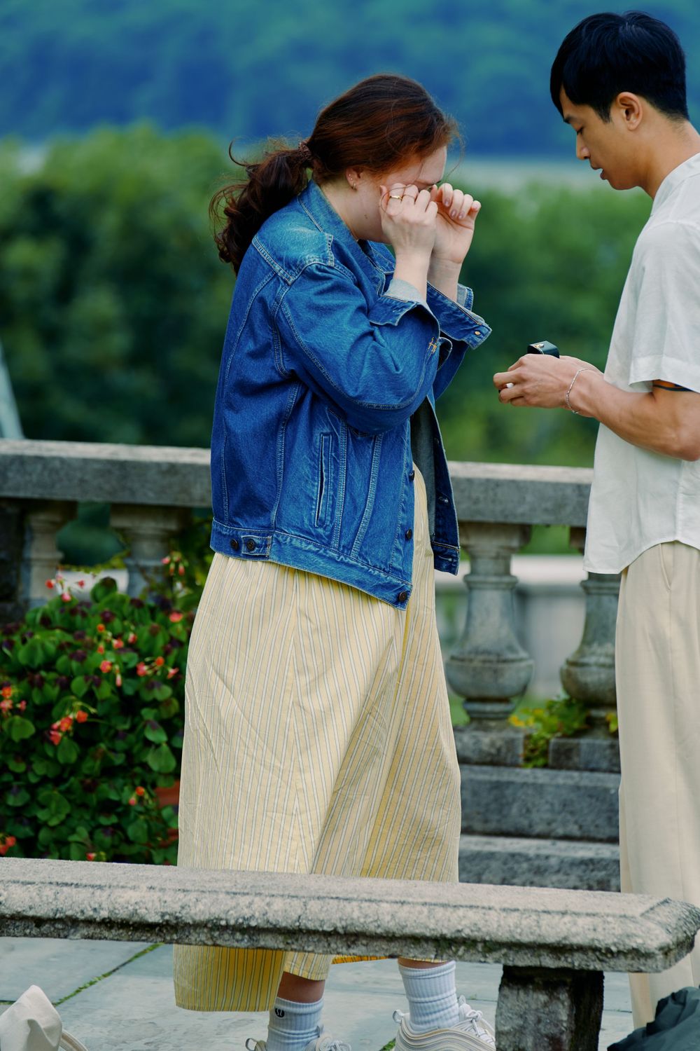 A couple shares an emotional moment on a stone balcony with a green mountain backdrop. Wave hill garden