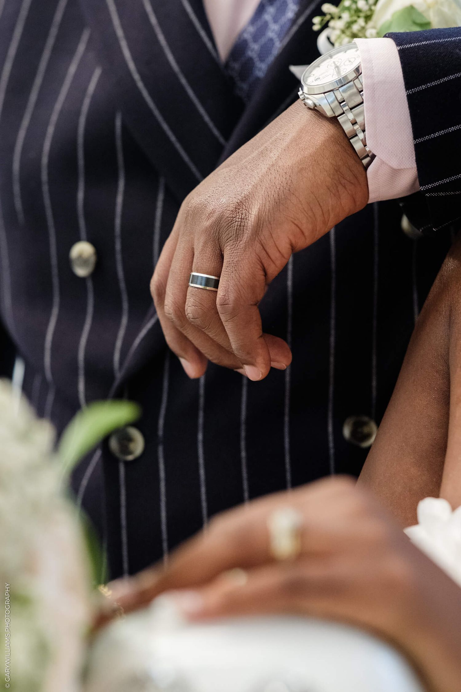 Close-up of hands wearing formal attire showing a silver wedding band ring and bracelet at a special event.