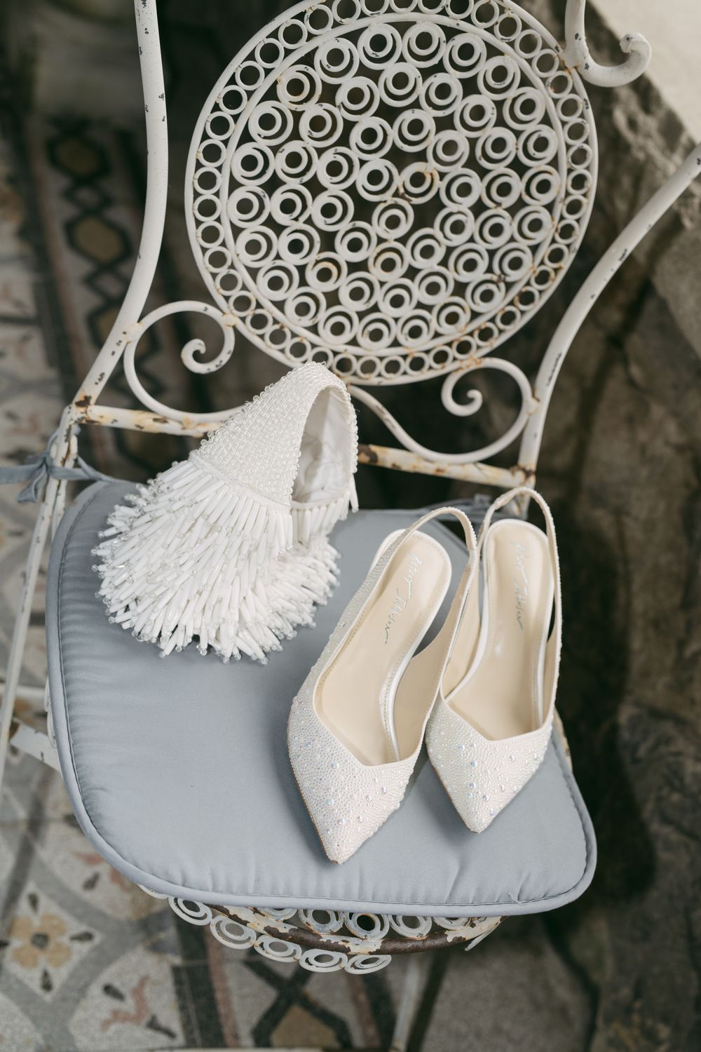 Delicate white lace wedding shoes displayed on an ornate vintage chair with decorative metalwork.