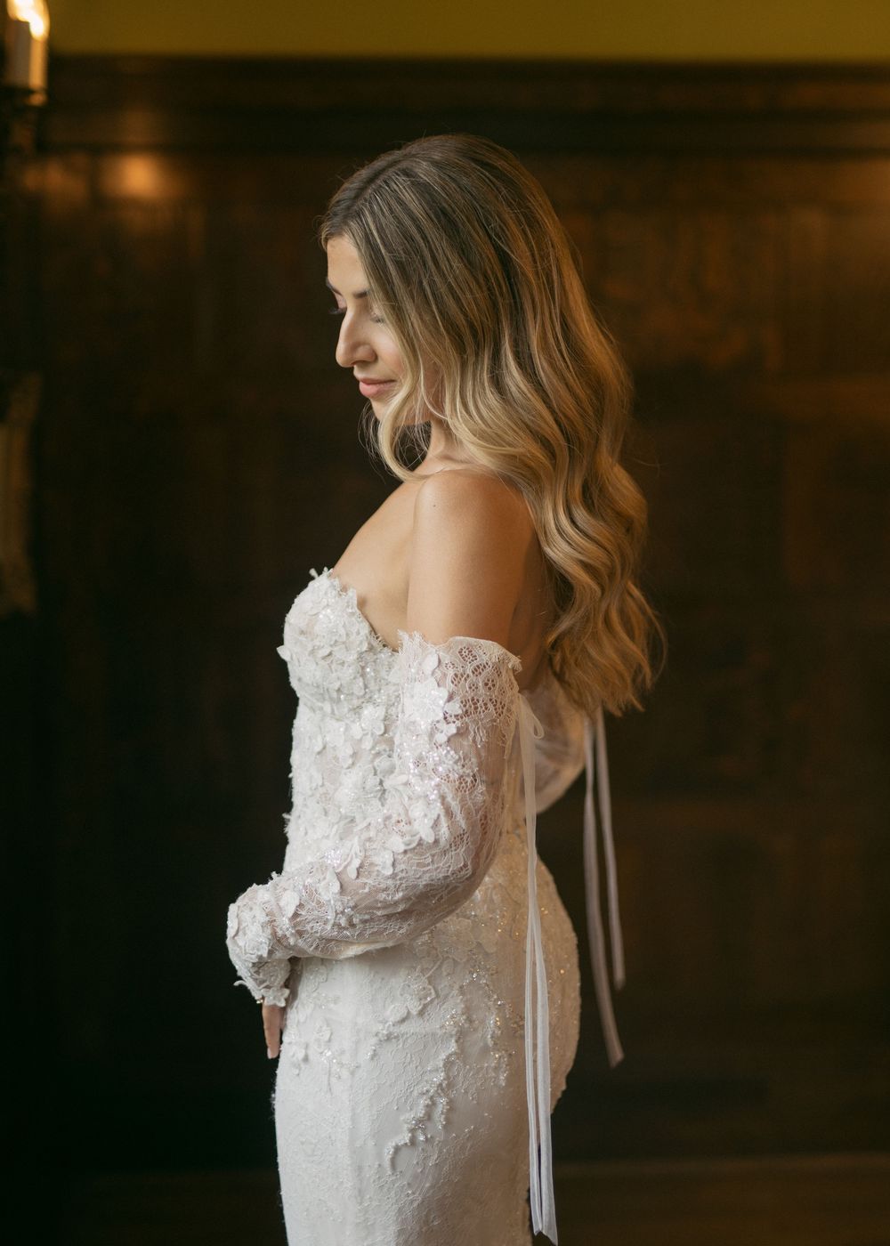 Close-up of delicate lace details on white wedding dress against dark background.