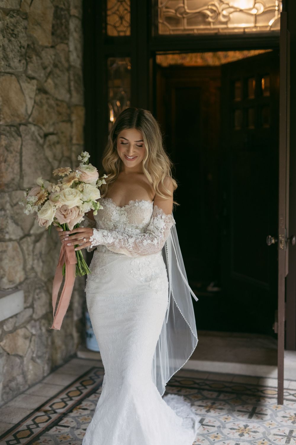 Bride holding white floral bouquet while standing in stone archway.