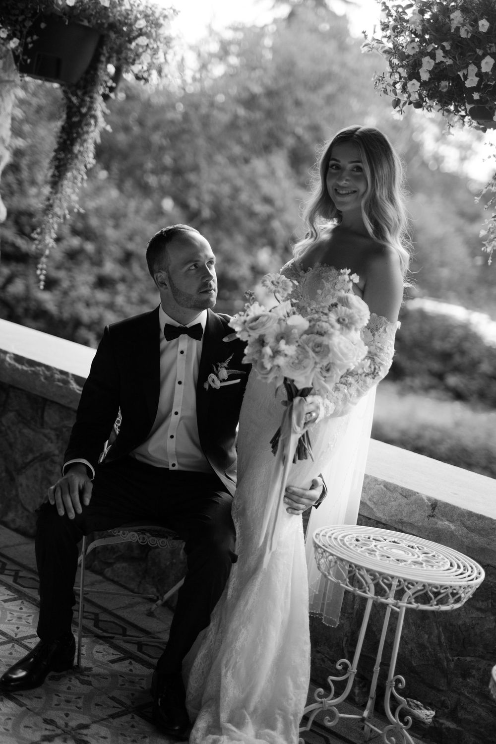 A couple sits intimately on an outdoor patio with white garden furniture.