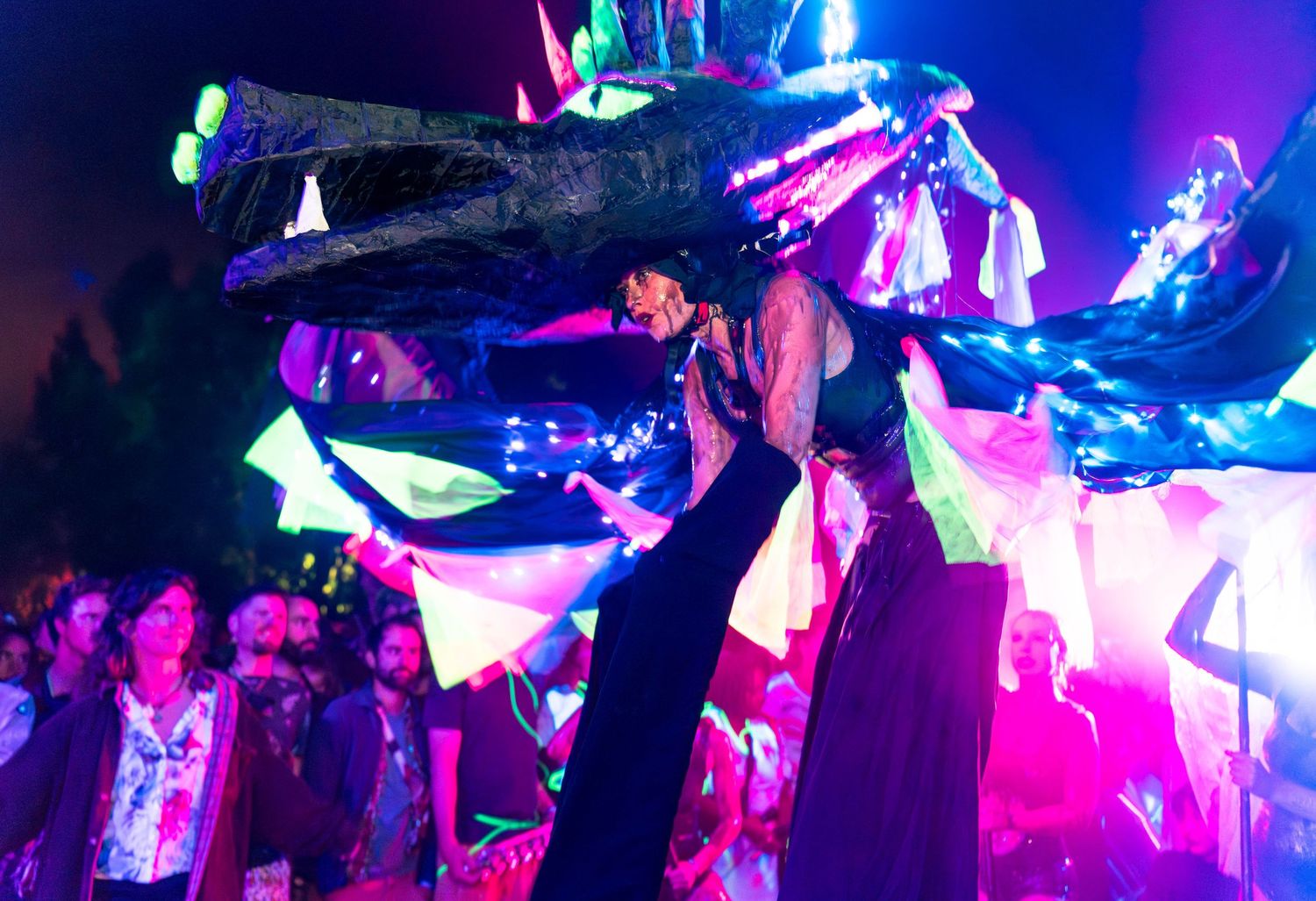 Close-up of a person dancing in a crowded venue, showing vibrant purple and neon party lighting.