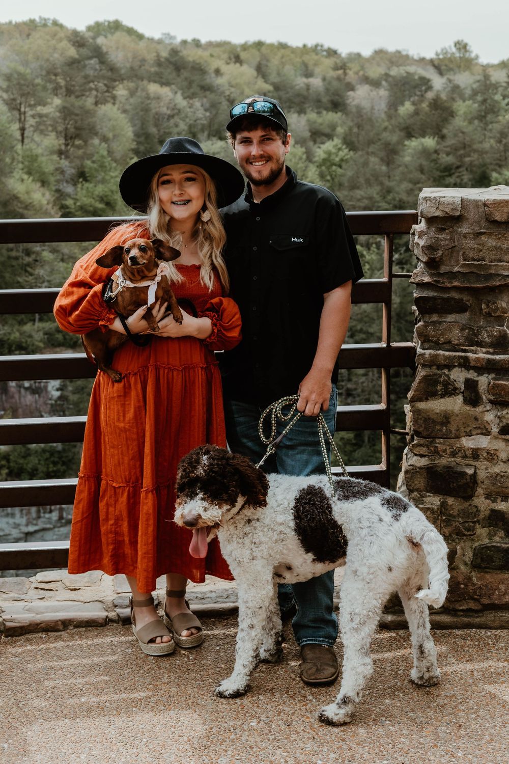 A couple enjoying an outdoor engagement session with their beloved shaggy dog on a stone bridge.