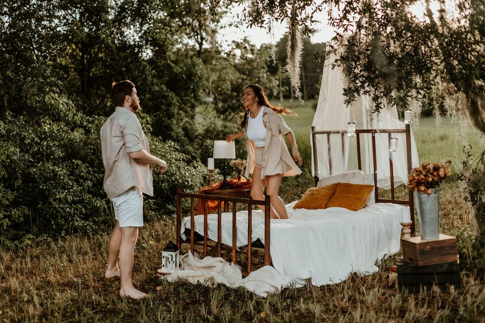 A romantic outdoor maternity photoshoot showing a couple snuggling on a white blanket in a sunlit field.
