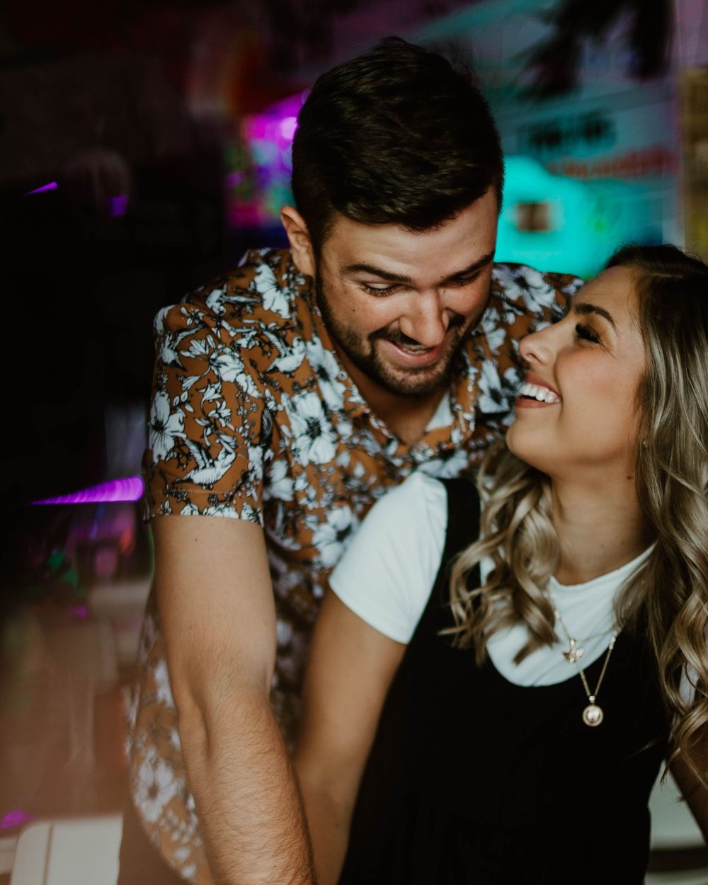 A couple shares an intimate romantic moment in a dimly lit venue with turquoise and purple ambient lighting.