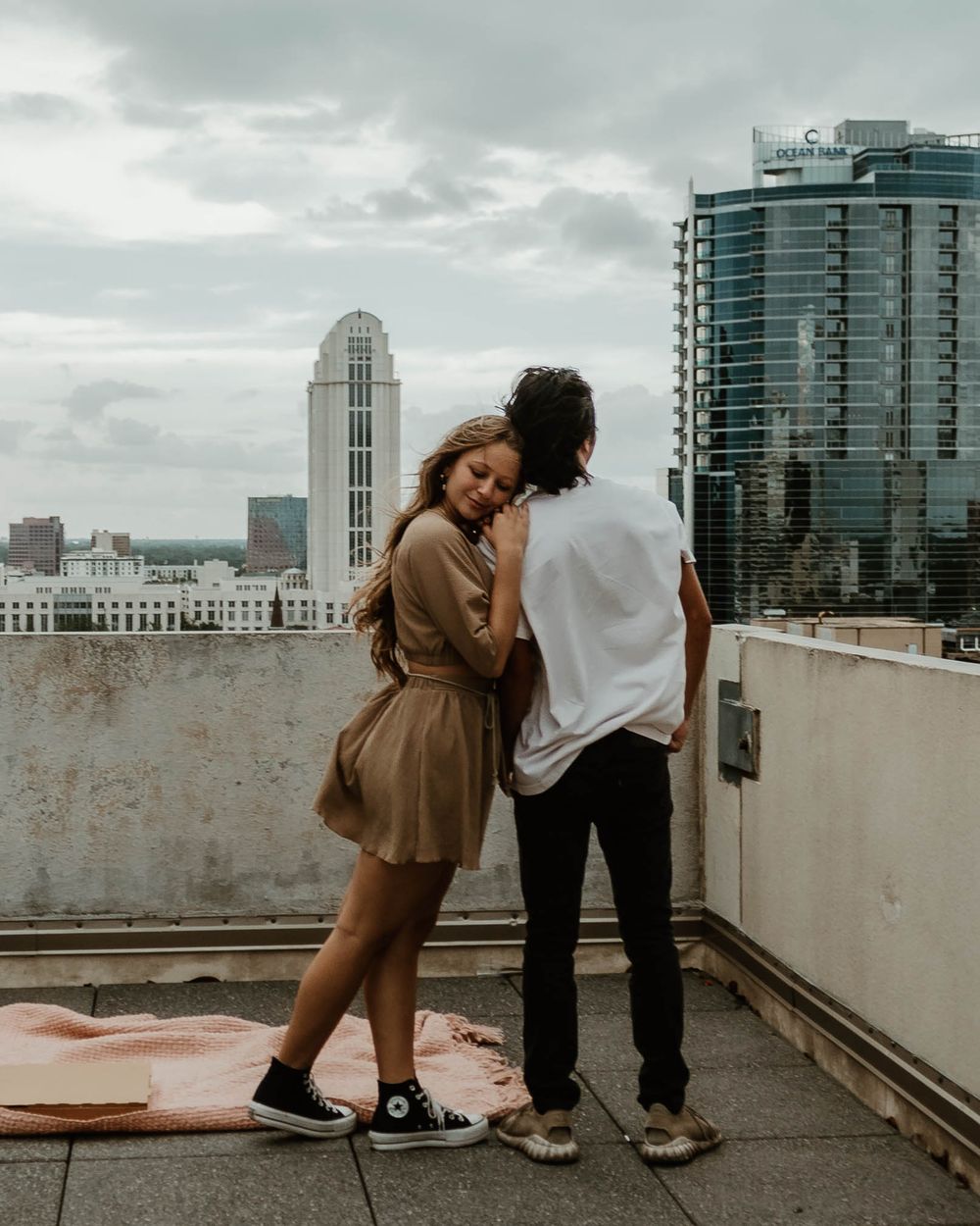 Romantic couple embracing on an urban rooftop with modern city buildings in the overcast background.