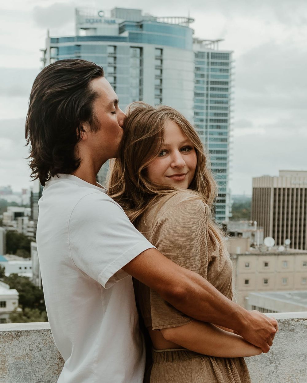 Couple embracing on an urban rooftop with modern skyscrapers visible in the skyline.