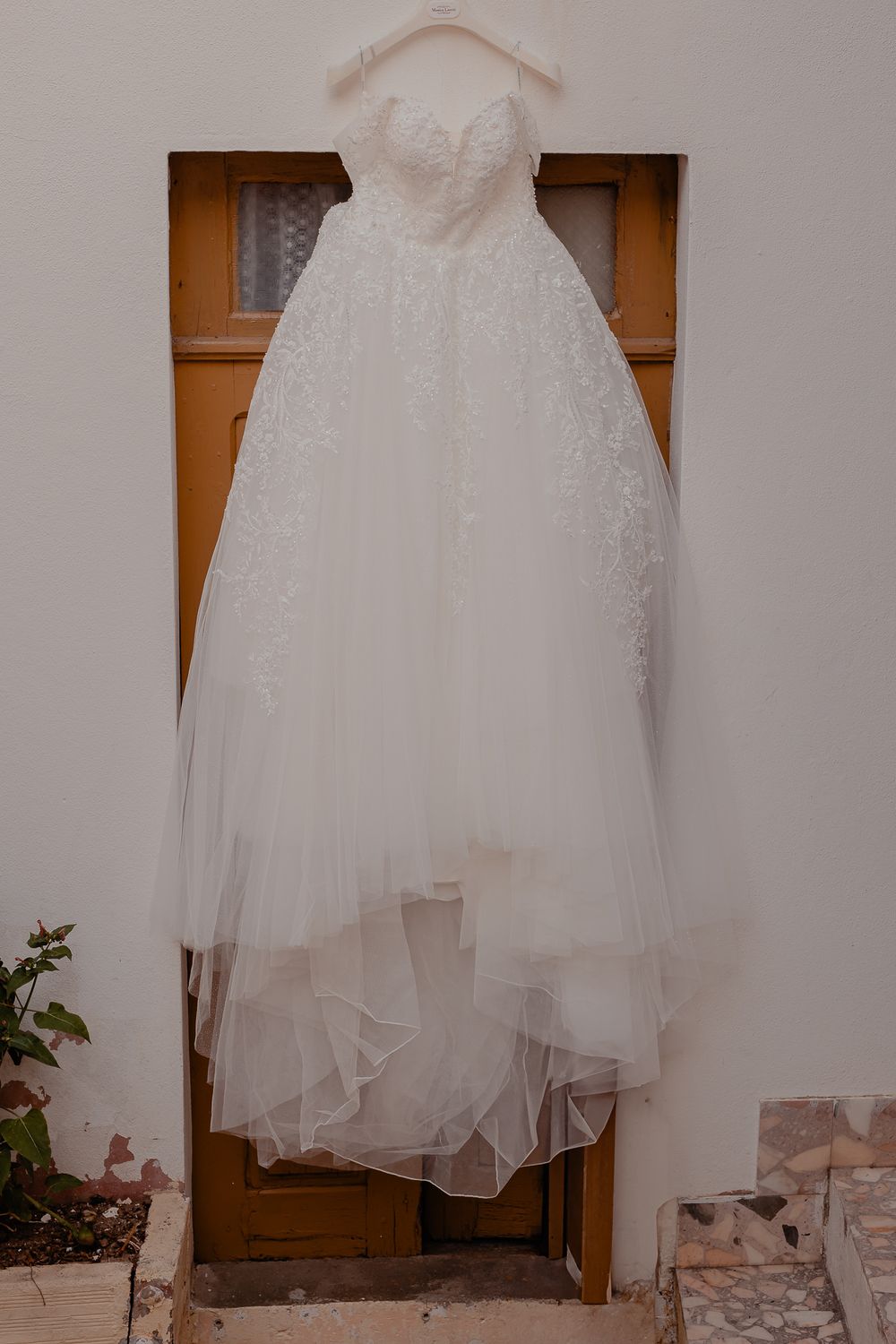 Elegant white flower girl dress hanging against wooden door.