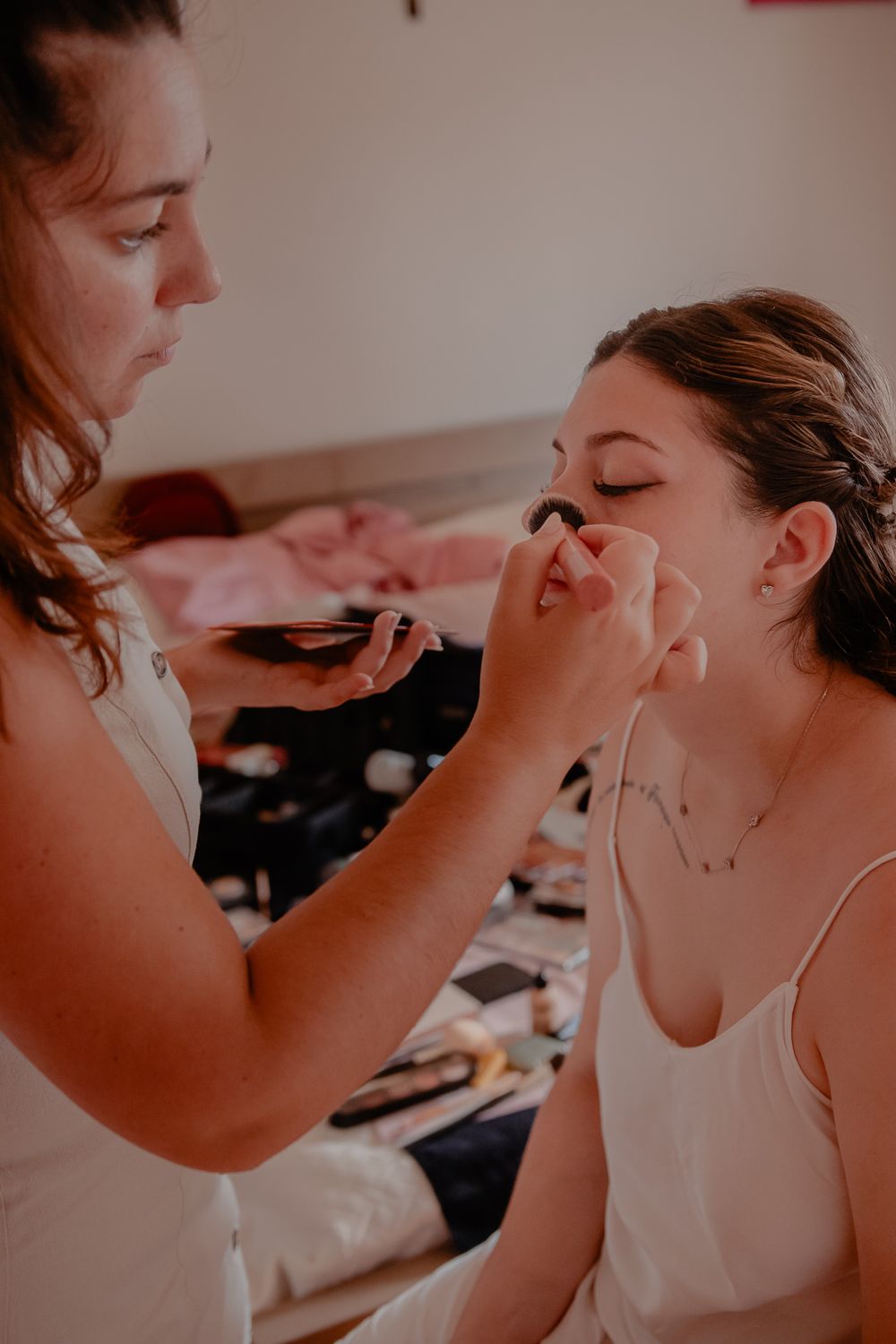 Professional makeup artist applying cosmetics during bridal preparation in soft lighting.
