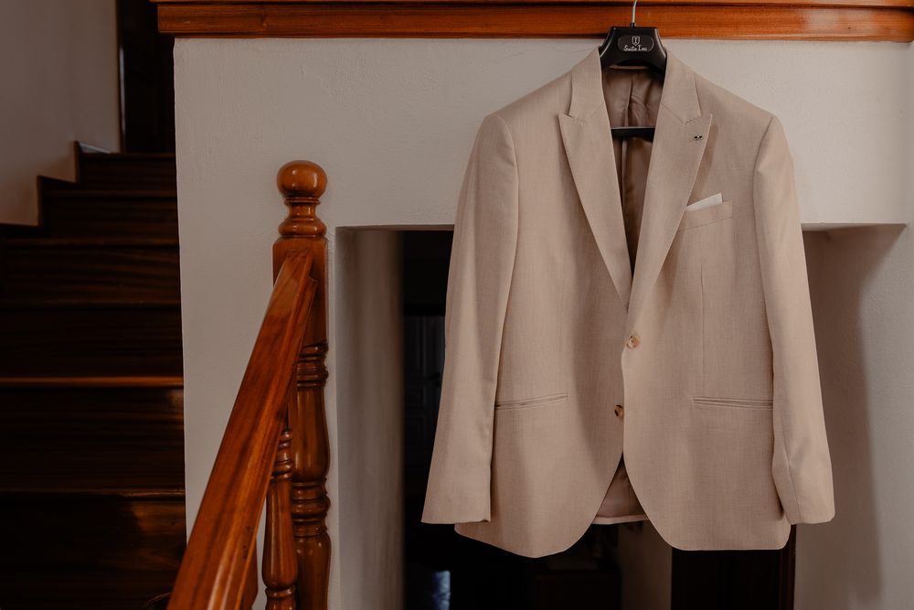 Light beige suit jackets hanging neatly on wooden hangers against a neutral wall.