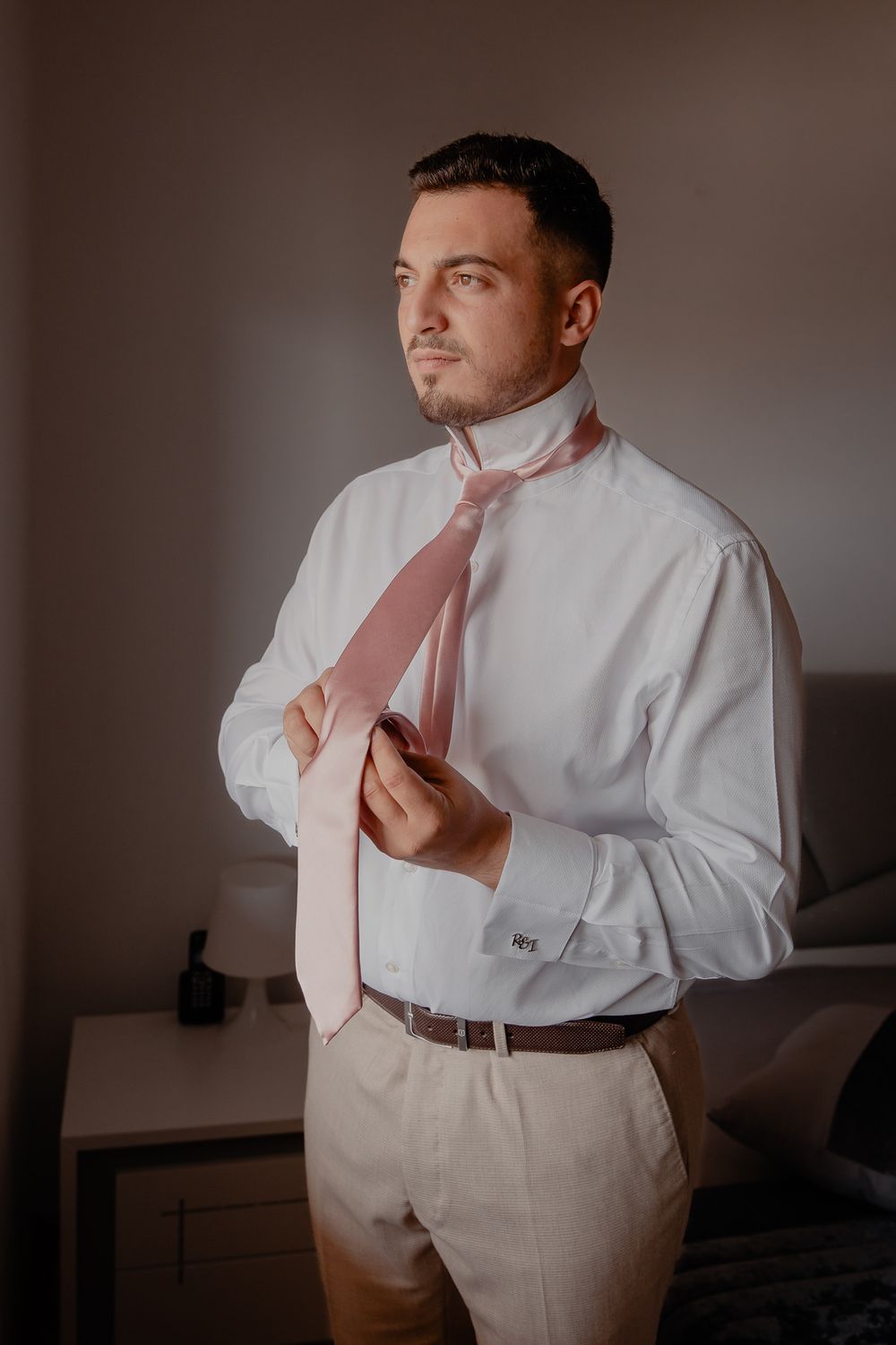 Man adjusting a pink tie while wearing a white dress shirt and khaki pants.