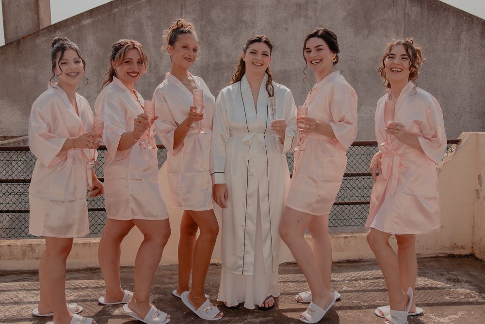 Wedding party wearing matching white robes posing together in natural light.