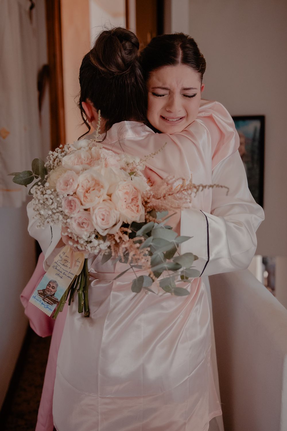 Wedding party members in white robes admire beautiful blush pink bouquets.