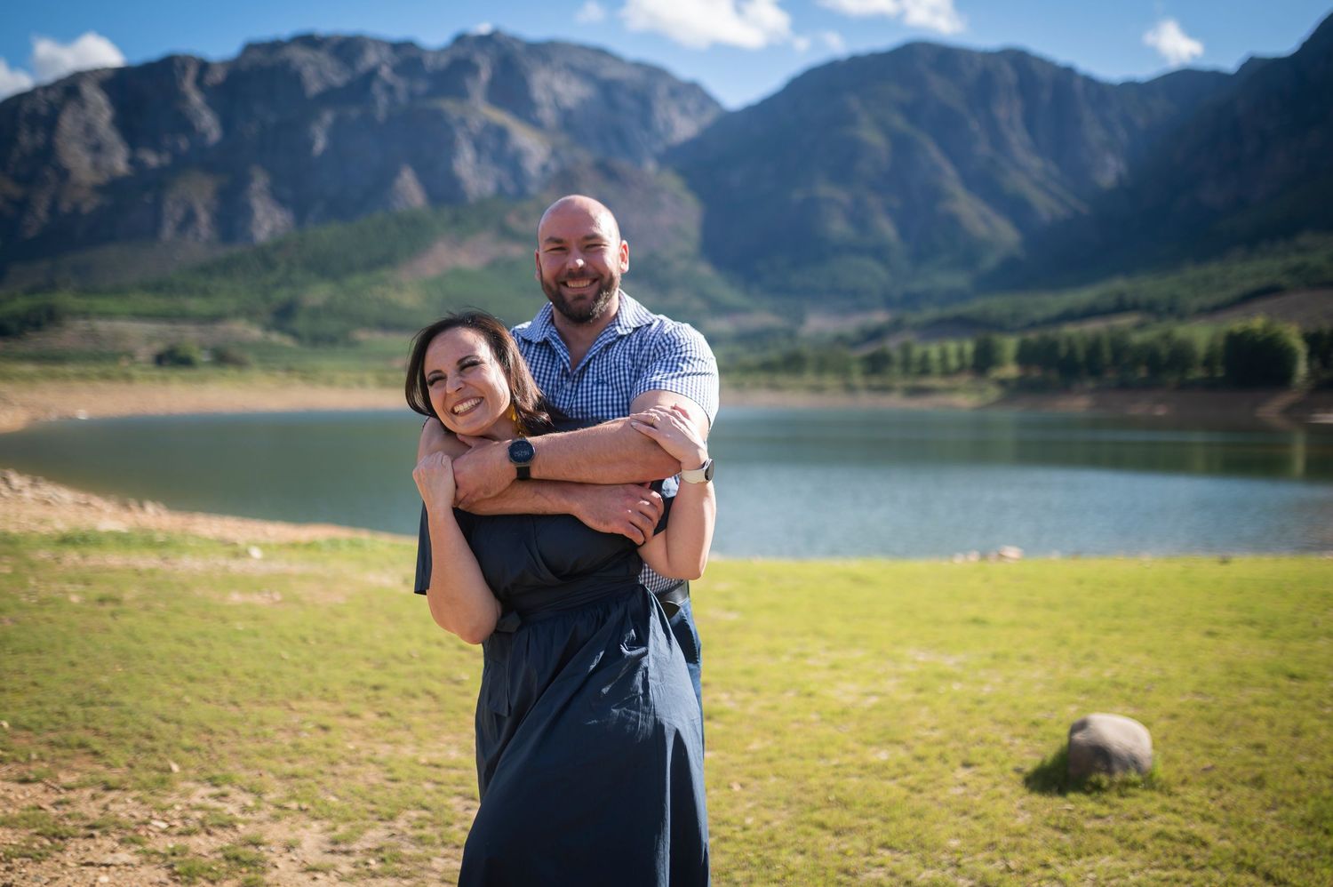 People taking engagement photos against a stunning backdrop of mountain peaks and a scenic lake.