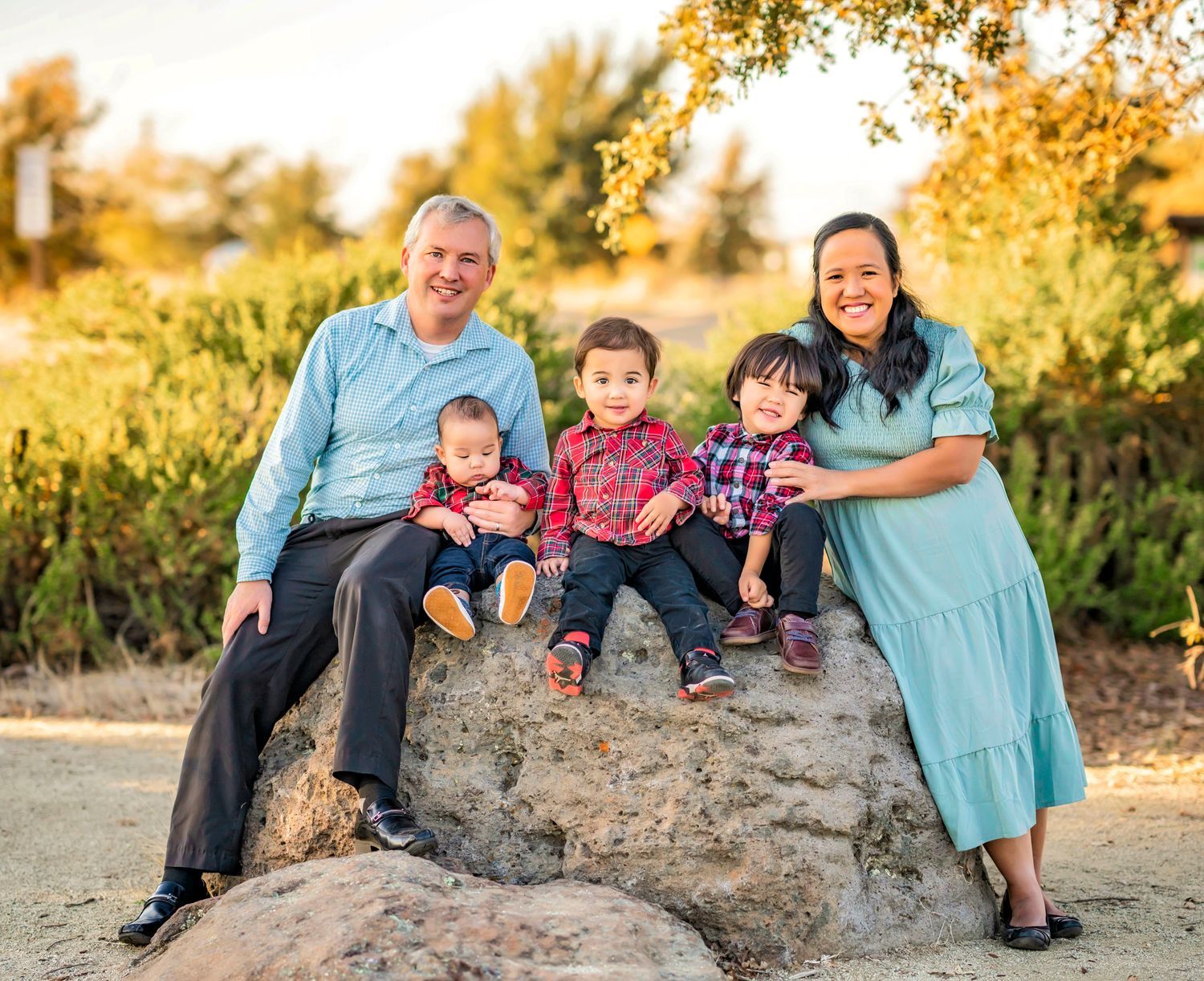 A group of five people sit together on a large rock during golden hour sunset in a natural outdoor setting.