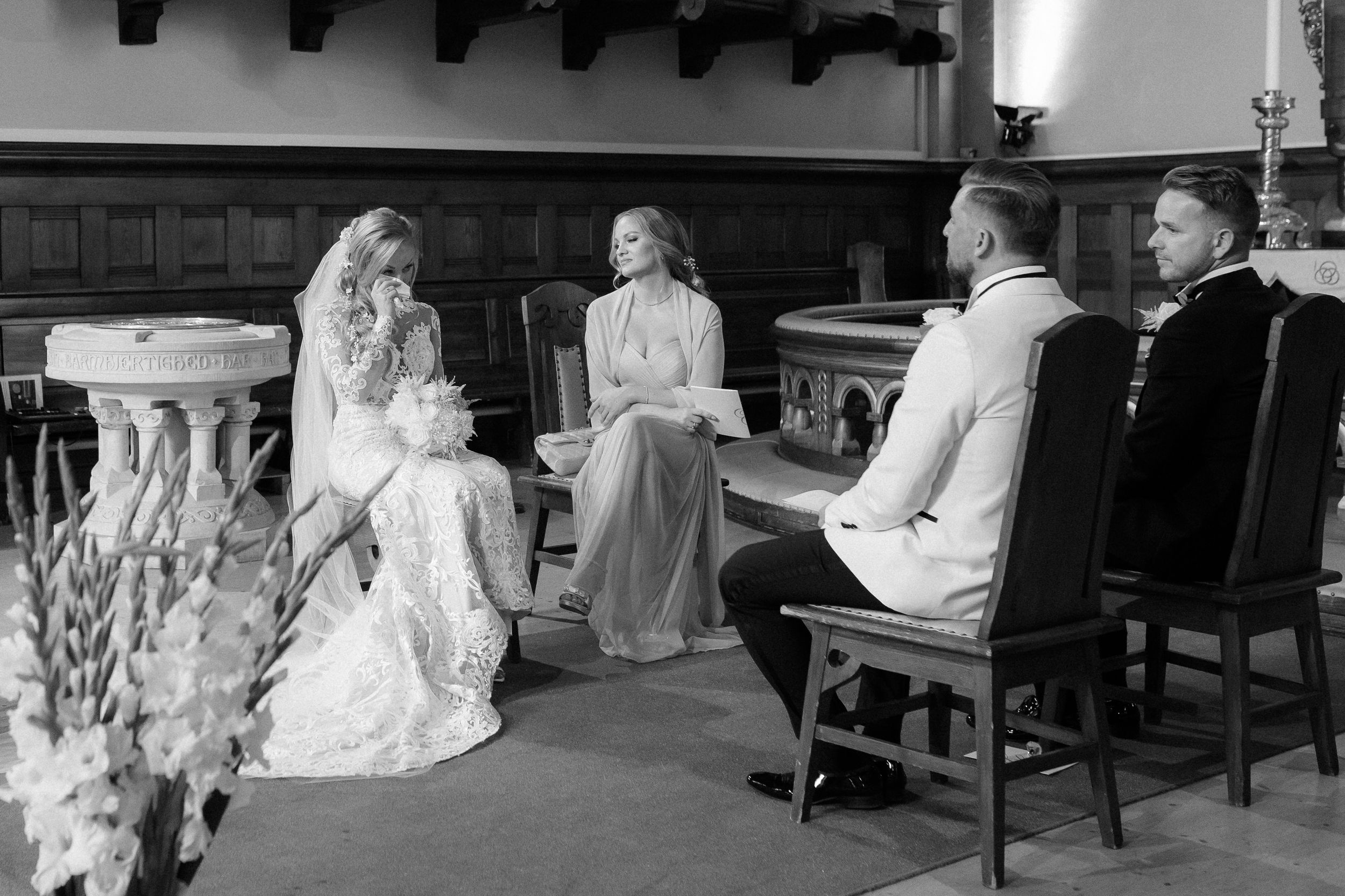 Wedding party seated at a long wooden table in a rustic indoor venue.