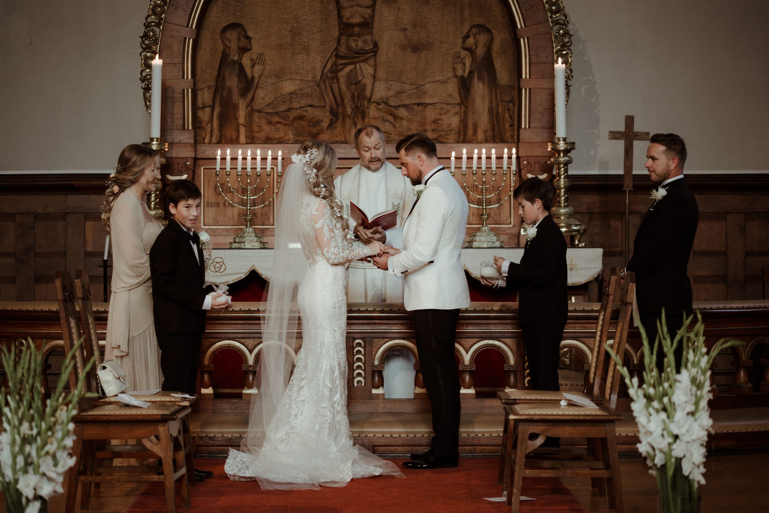 A romantic wedding ceremony unfolds in an elegant church setting with white floral arrangements and candles.