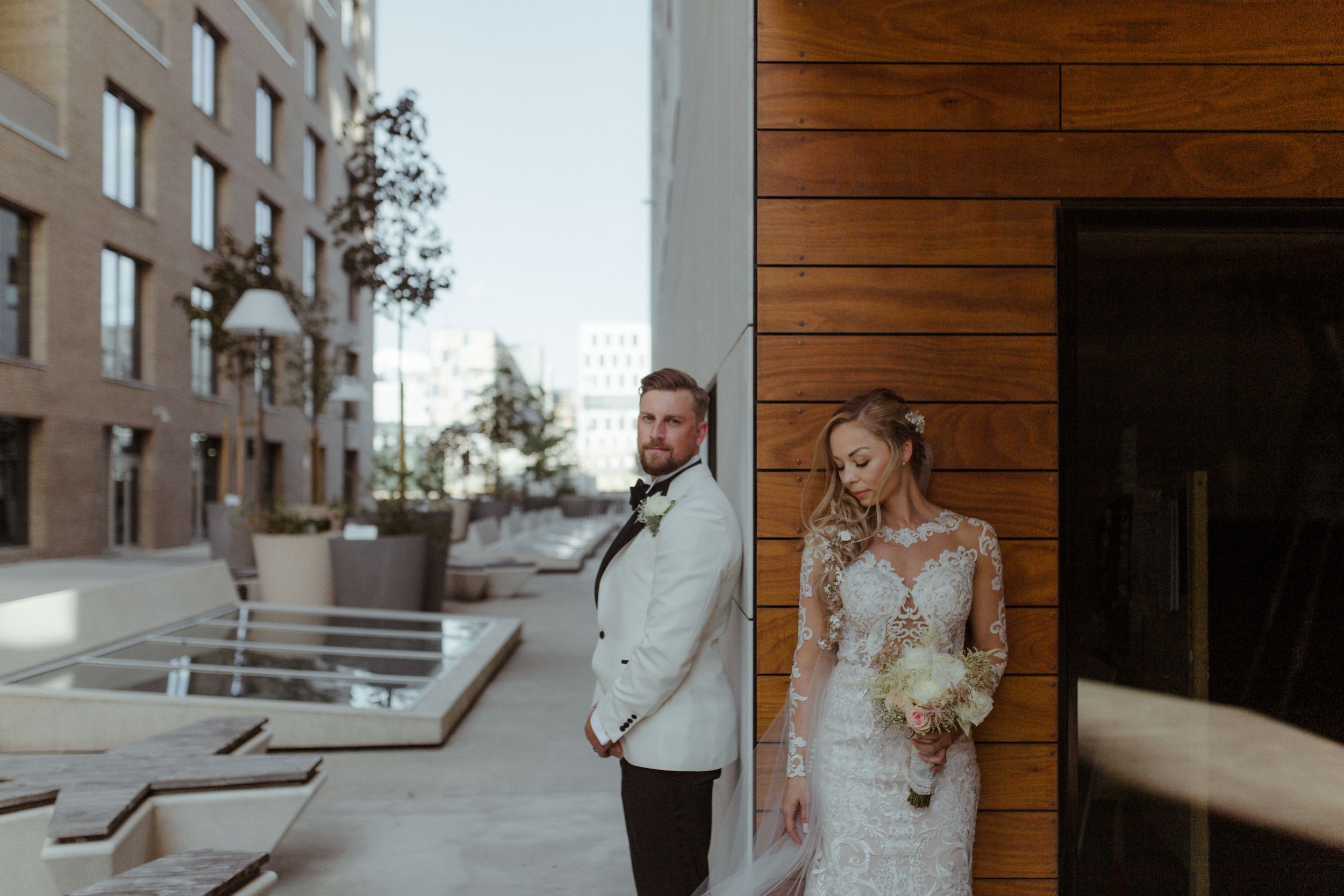 A modern wedding couple stands in a stylish wooden-paneled hallway.