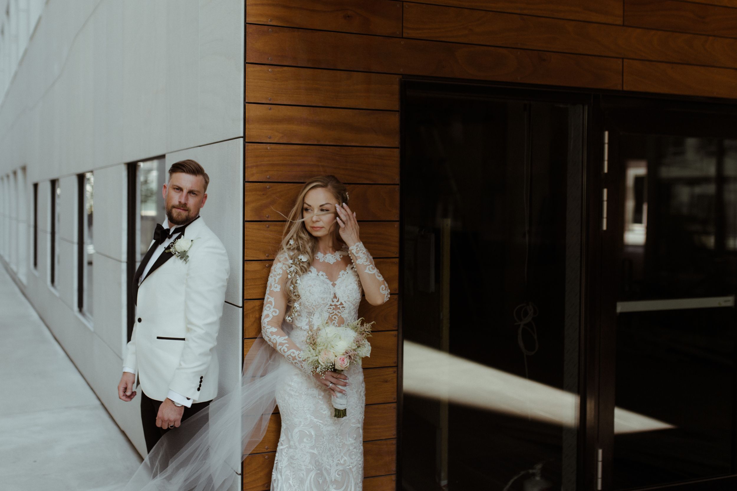 A couple poses against a modern architectural backdrop with wood paneling and white walls on their wedding day.