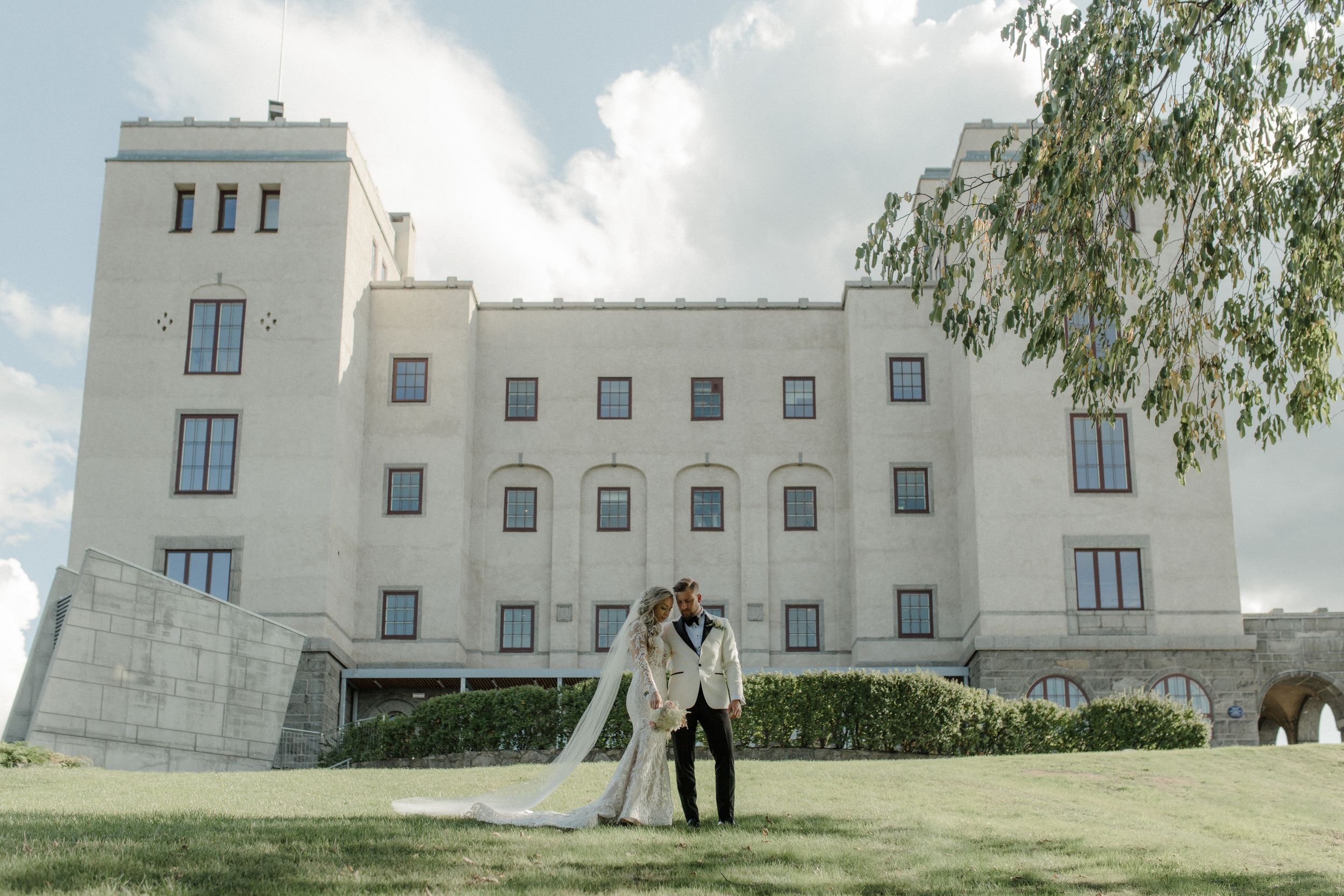 Elegant white mansion on a hill against cloudy sky creates dramatic wedding backdrop.